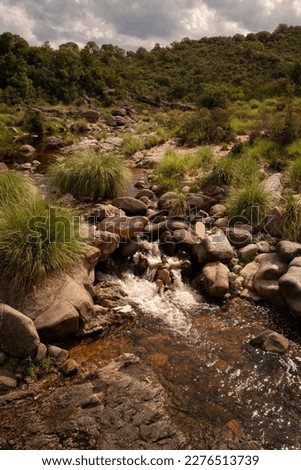 Vacations. Portrait of a young woman wearing a bikini, laying under a waterfall in the rocky river. The forest and mountains in the background.  Royalty-Free Stock Photo #2276513739