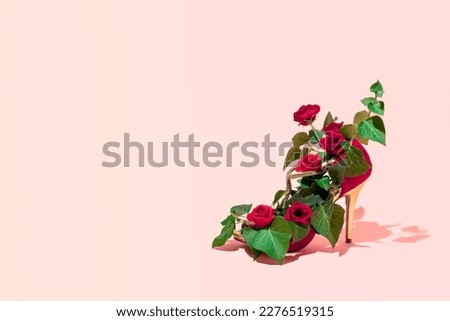 High heel dancing shoe decorated with fresh green heart shape  leaves and red roses, creative aesthetic nature inspired fashion trend, pastel pink background.