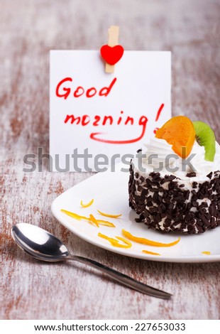 beautiful cup-cake with fruits and cream  on white saucer and note with love on old wooden surface 