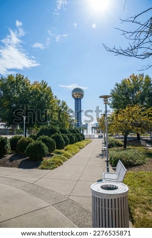 a gorgeous autumn landscape at World's Fair Park with a water fountain, autumn trees, lush green trees, the Sunsphere with blue sky and clouds in Knoxville Tennessee USA