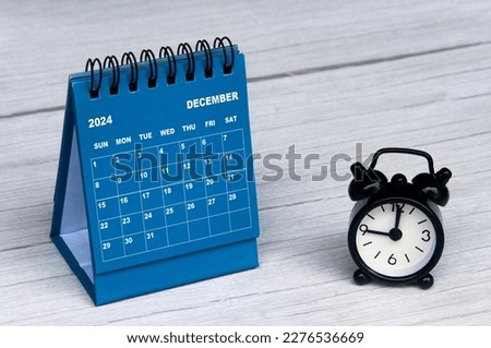 December 2024 calendar on wooden desk and alarm clock with customizable space for text. Monthly calendar concept and copy space.
