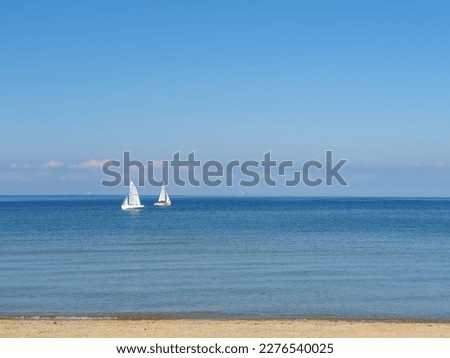 View of two sailboats moving away from one another seen from beach shoreline