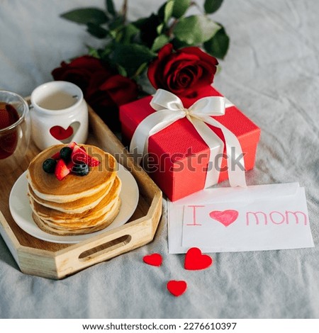 Mother's Morning breakfast on wooden tray with greeting card I love you mom, bouquqet of red roses, gift present box. Square image