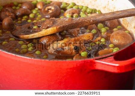 Sausage casserole in a red casserole dish, with potato, mushrooms, tomatoes, peas and onion, in a beef stock.