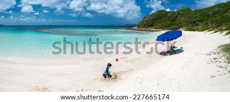 Kids playing on picture perfect beach with blue umbrella, white sand, turquoise ocean water and blue sky at tropical island in Caribbean
