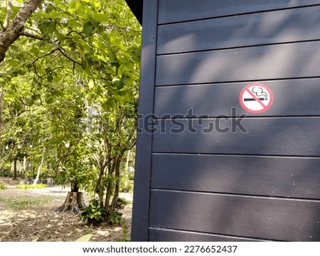 No smoking sign in the corner of the dark wooden building there is a garden with shaded trees on the left side