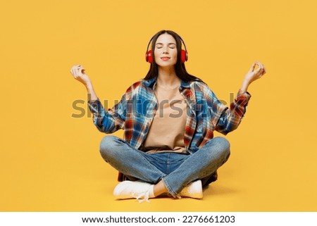 Full body young woman wearing blue shirt beige t-shirt headphones hold spreading hands in yoga om aum gesture relax meditate try to calm down listen music isolated on plain yellow background studio