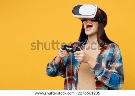 Young excited woman wear blue shirt beige t-shirt hold in hand play pc game with joystick console watching in vr headset pc gadget isolated on plain yellow background studio. People lifestyle concept