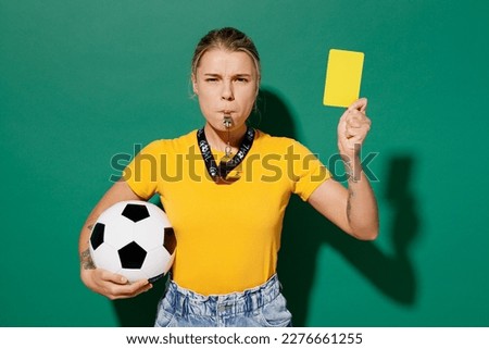 Young sad woman fan wear yellow t-shirt cheer up support football sport team hold soccer ball yellow card propose player leave field blow whistle watch tv live stream isolated on dark green background Royalty-Free Stock Photo #2276661255