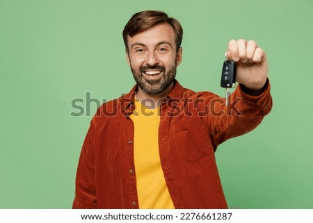 Elderly happy smiling man 40s years old he wears casual clothes red shirt t-shirt hold in hand car keys fob keyless system give stretch arm to camera isolated on plain pastel light green background