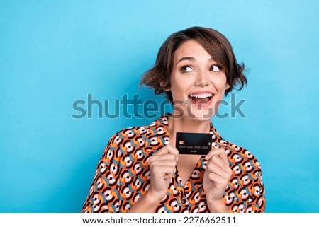Photo of adorable excited woman wear print blouse rising credit card looking empty space isolated blue color background