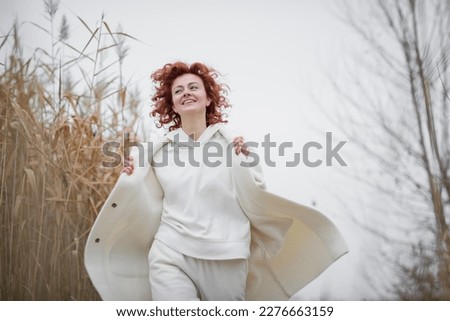 Pretty young woman in trendy white clothes poses in motion against the backdrop of an autumn landscape with dry reeds Royalty-Free Stock Photo #2276663159