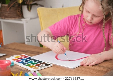 activities with a child concept, a cute girl with blond long hair draws a rainbow on paper, a preschooler paints with watercolors