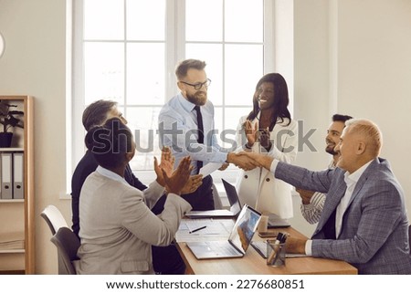 Two men shaking hands celebrating success, making a deal, business achievement or signing a contract on their workplace. Group of business people in office applauding to their coworkers.