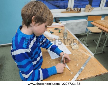  boy with red hair in a blue sweater is making a boat out of Styrofoam Royalty-Free Stock Photo #2276723133