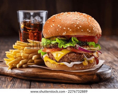 Tasty cheeseburger or hamburger, glass of cola and french fries on wooden tray close-up.
