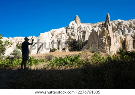 Traveling in Cappadocia, a tourist taking pictures of unusual rock formations in the Rose valley of Goreme National Park, silhouette of a man in the shadow, Turkey nature