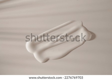 A white creamy drop of skin care cream. A smear of cosmetic cream with shadows in the sun. Smooth smear on a light background with a space for copying. Layout for the design. High quality photo