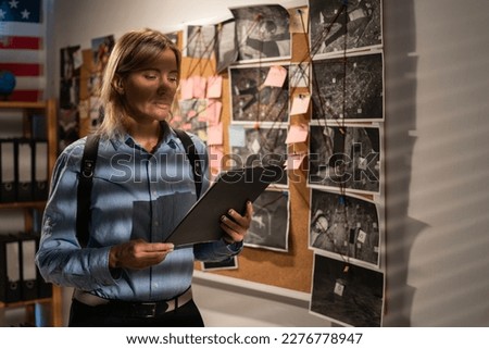 Woman private agent looking at crime investigation board holding clipboard, chasing serial killer. Copy space Royalty-Free Stock Photo #2276778947