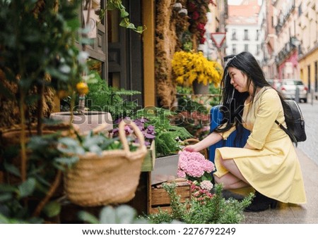 A tourist girl with her suitcase enjoying a flower shop in the street.