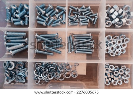 View of the transparent storage box, nuts, screws, screw boxes, small construction objects. Many storage compartments are full of accessories with screws, nuts, bolts neatly arranged.