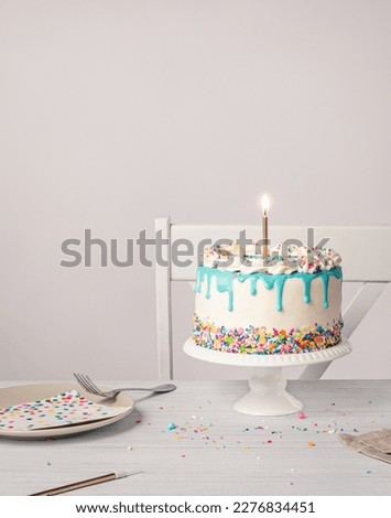 Birthday party with vanilla buttercream Cake, lit gold candle and confetti sprinkles on a light grey white background