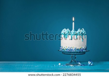 White cake with one lit birthday candle on a blue background Royalty-Free Stock Photo #2276834455