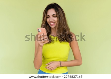 Young woman in casual wear isolated on green background looking at phone screen with big smile reading message