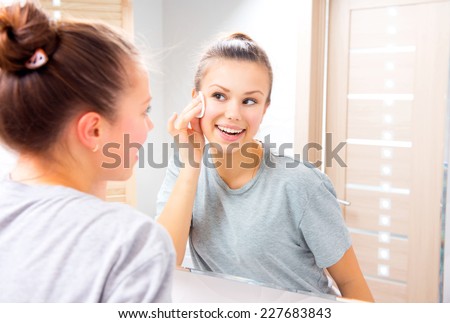 Fresh clean skin. Beauty teenage girl cleaning her face with cotton pad at home. Young happy brunette woman removing makeup from her face enjoying her skin and smiling at the mirror. Beauty skin care Royalty-Free Stock Photo #227683843