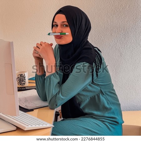 A happy young Muslim woman in hijab working on a laptop at home office. High quality photo