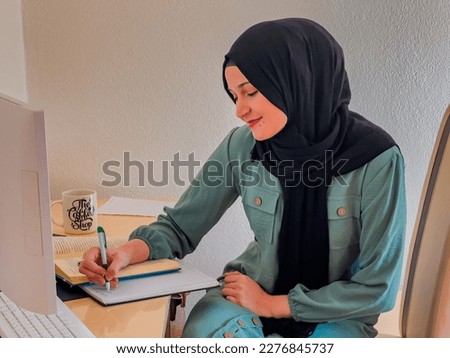 A young Muslim woman works on a laptop and writes in a notebook. High quality photo