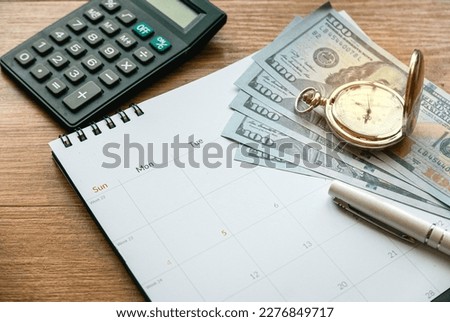 Tax time and saving money and financial planning concept. Calculating monthly expenses. Finance debt collection deadline. Money, calendar, clock and calculator on wooden table.
