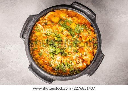 Delicious Brazilian fish moqueca with tomato, onion, olive oil, coriander and orocum seed. Made in clay pot on white table and black background. Top view. Royalty-Free Stock Photo #2276851437