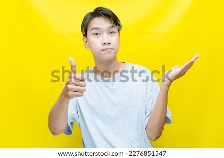 colored hair a young Asian man in gray tshit pointing, promoting, displaying, and offering something good with his hands. man advertising stuff happy and joyfully