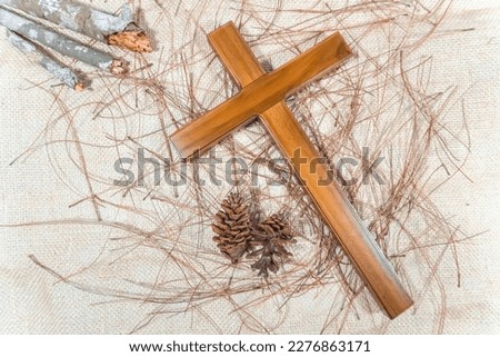 A wooden cross and dry woods used by Catholic Christians on Maundy Thursday and Good Friday on burlap background with pine leaves and pinecones. Royalty-Free Stock Photo #2276863171
