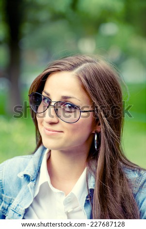 Happy girl in clear glasses looking at camera. Long haired brunette outdoors on the nature background. Toned image, film color imitation.
