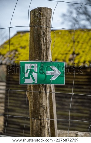 Green Emergency Exit Sign at a Wildlife Park, Amusement Park hanging on a tree trunk in front of a metal fence, vertical shot