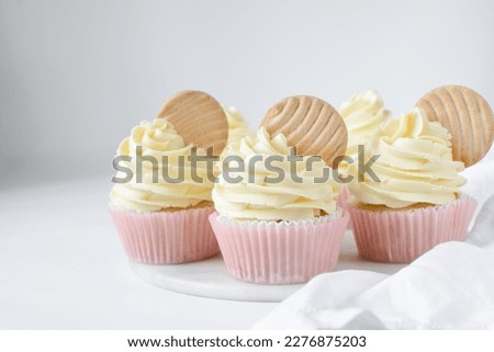 Pink cupcakes with tall american buttercream swirl and cookie garnish, cupcakes in pink liners with a tall vanilla buttercream and a cookie, birthday cupcakes on a white background Royalty-Free Stock Photo #2276875203