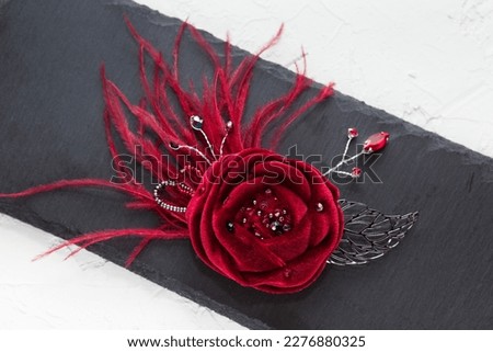 Handmade velvet vinous rose flower broach with feathers, lying on the dark gray stone background, top flat view Royalty-Free Stock Photo #2276880325