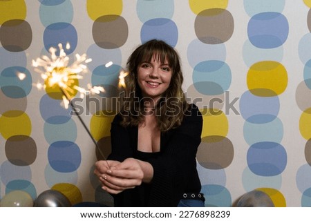 Young Woman Sitting with a Sparkler Against Colorful Background
