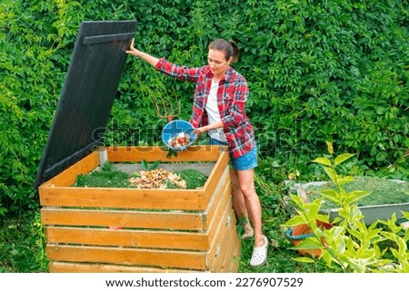 Food waste in a compost bin. A woman in a plaid shirt throws kitchen waste into a DIY compost bin. Aging of compost for its introduction into the soil to improve its structure and fertility.  Royalty-Free Stock Photo #2276907529