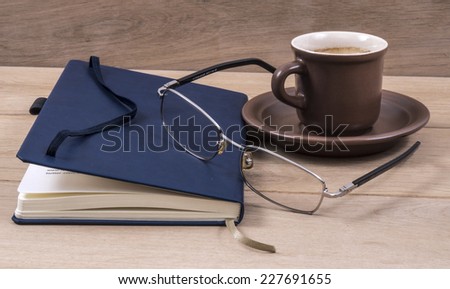 Image of notebook closed coffee cup pen and glasses.