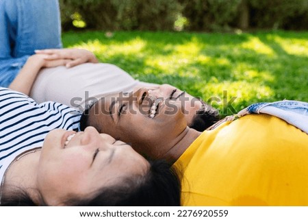 Three multiracial young women friends having fun together outdoors. Female friendship concept with small group of diverse teenager girls laughing while lying on grass in public park