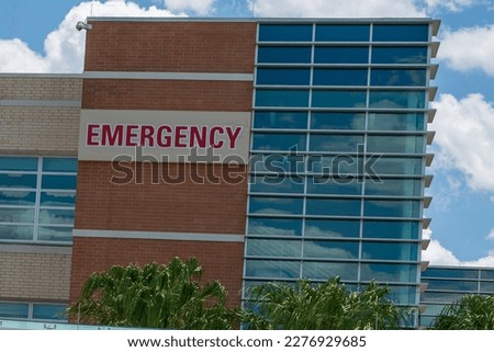 Orlando, Florida, US-March 2023: Emergency Center entrance to a hospital. A medical hospital's emergency department sign is made of red glass. The sign is attached to a clear glass building overhang