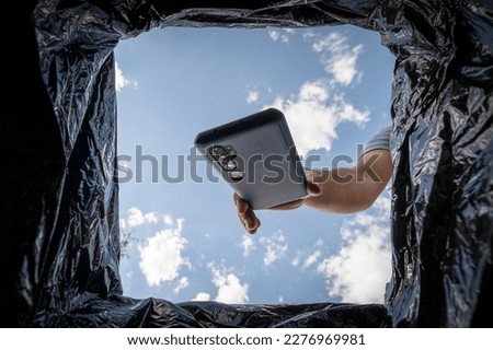 Young man throwing smartphone in litter bin outdoors. Recycling a broken smartphone. Royalty-Free Stock Photo #2276969981