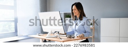 Woman Using Adjustable Height Standing Desk In Office For Good Posture Royalty-Free Stock Photo #2276983581