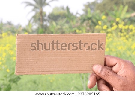 brown colored sign card on hand with mustard farm for any text