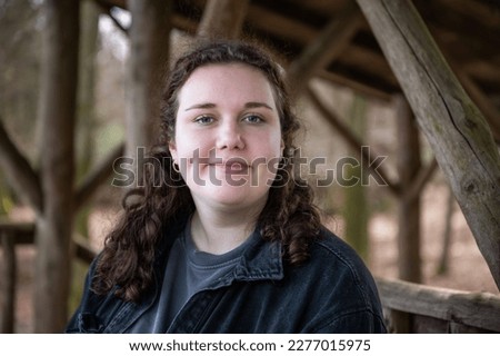 Close-up woman with brown curly hair smiling and looking at camera while sitting on a bench at a zoo viewing platform, Englischer Garten Eulbach