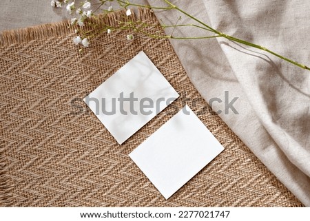 Two empty paper sheet cards and flower on a warm beige rug background, business template with mockup copy space