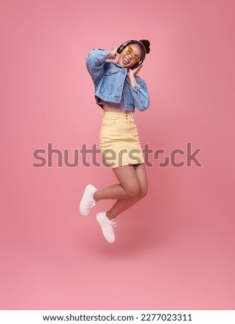 Funny young asian woman jumping isolated on pink background studio portrait. Listening music with headphones, dancing. People lifestyle concept.
